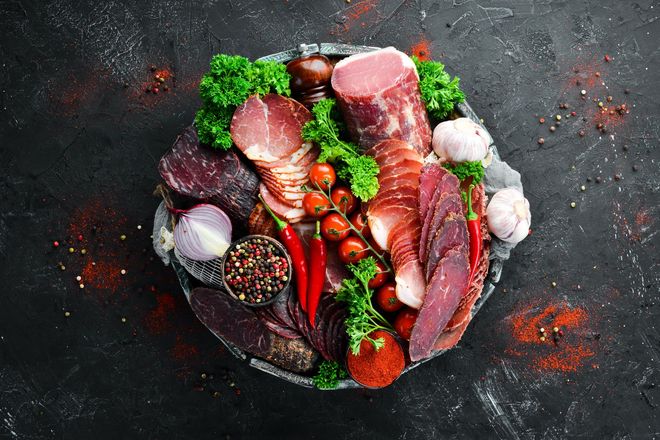 Assortiment de viandes crues, de fraises, de poivrons et d'épices disposés sur une surface à la texture sombre.