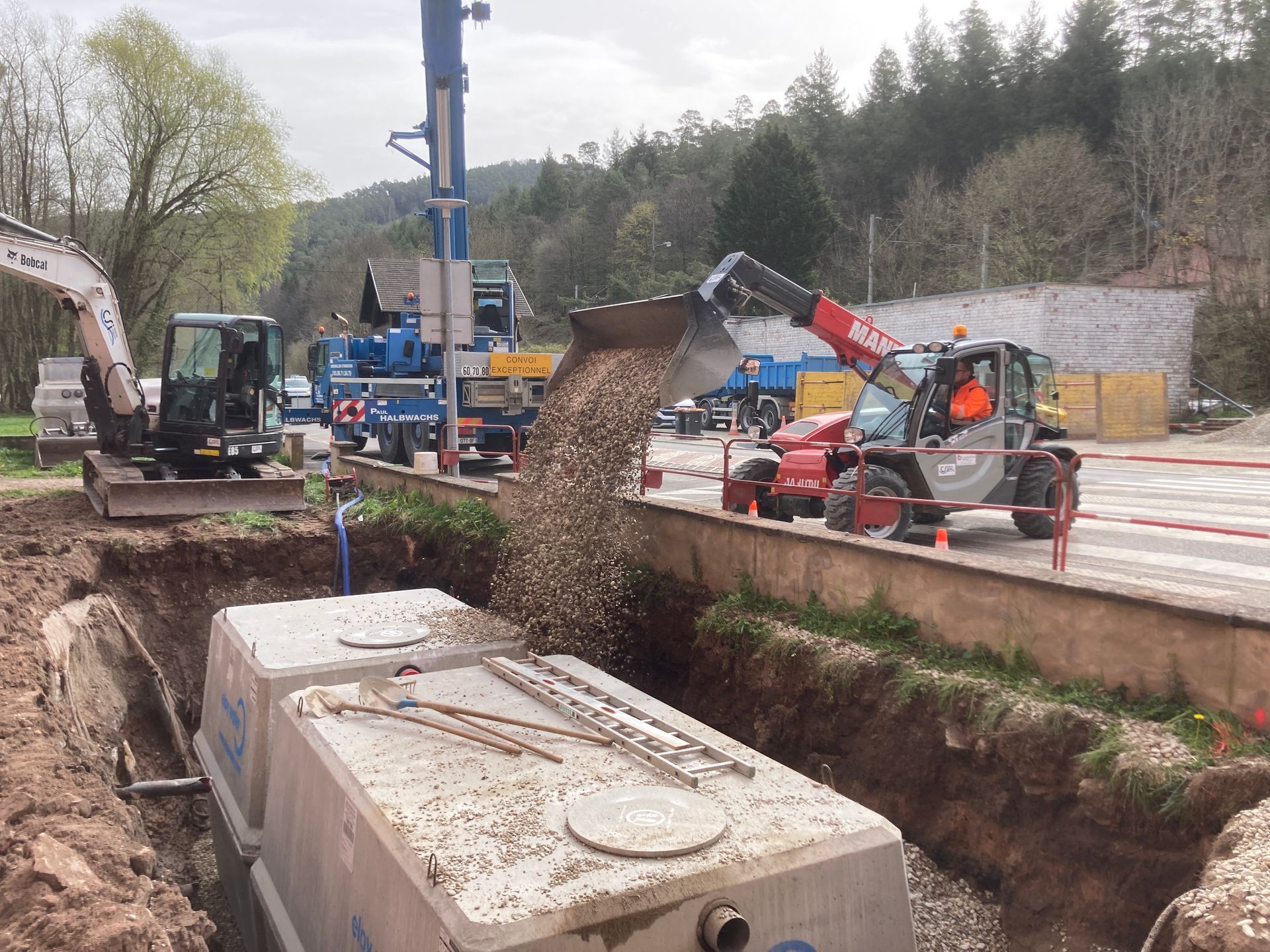 Un engin de chantier en train de verser de la terre et des cailloux sur une microstation dans un trou.