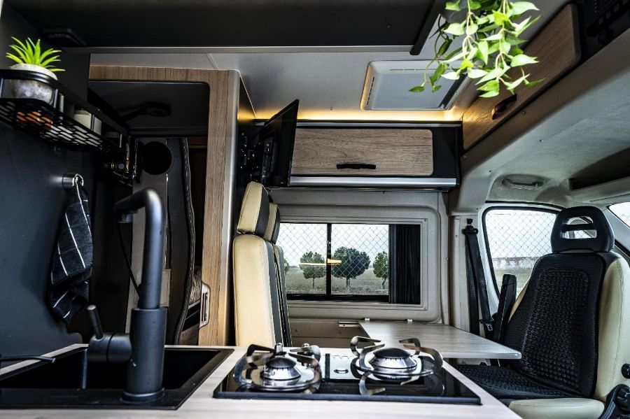 Interior de una furgoneta camper compacta con cocina, ventana y planta colgante.