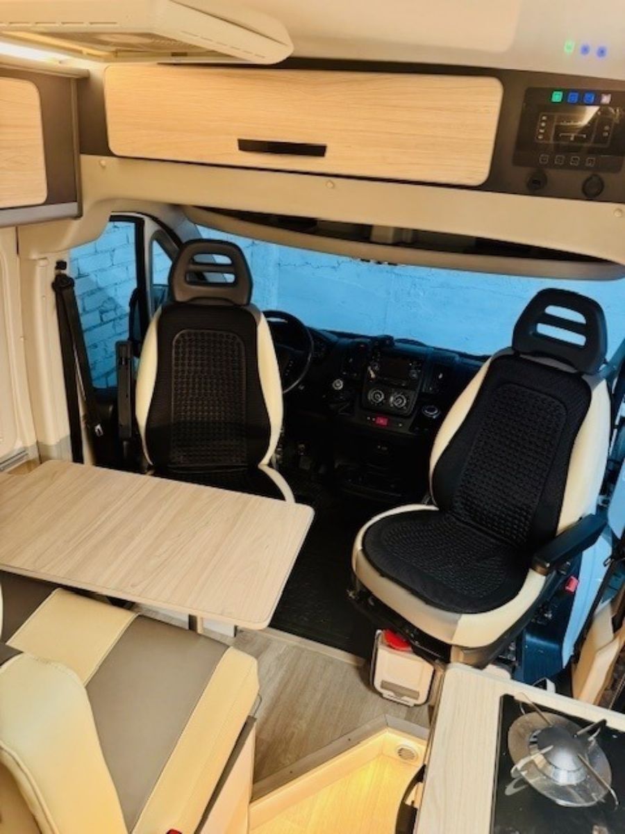 Interior compacto de autocaravana con dos asientos giratorios, una mesa y armarios superiores.