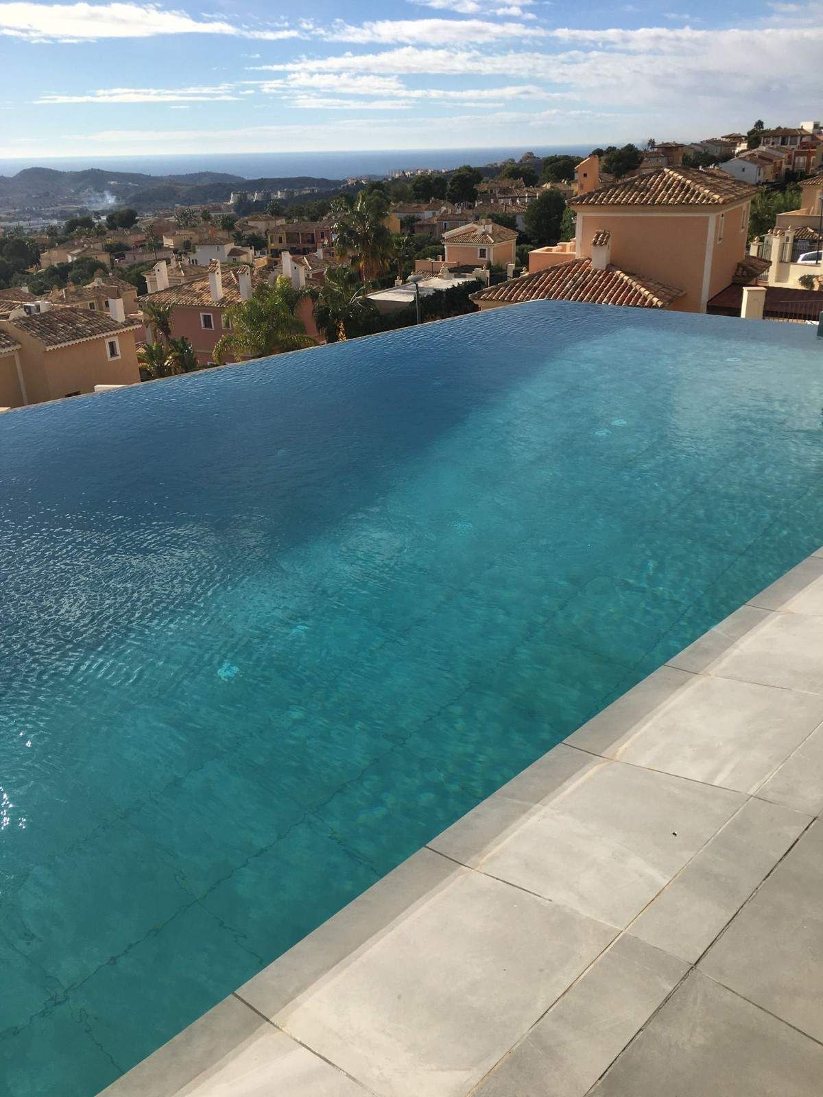 Piscina infinita con vistas a un pueblo con techos de terracota, agua azul y un cielo brillante.