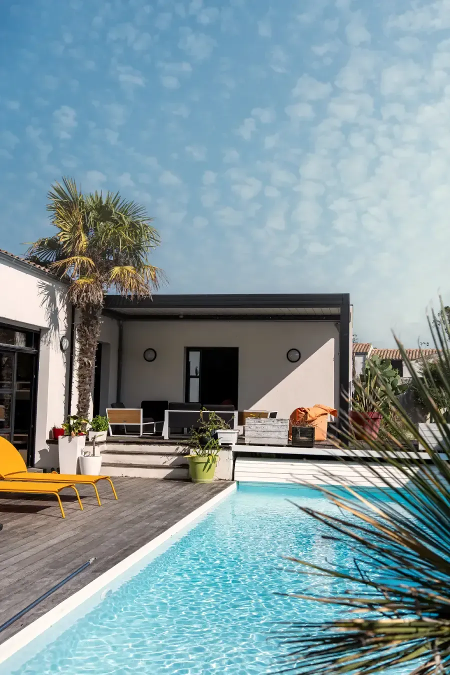 Patio junto a la piscina con piscina, tumbonas y edificio bajo un cielo azul.