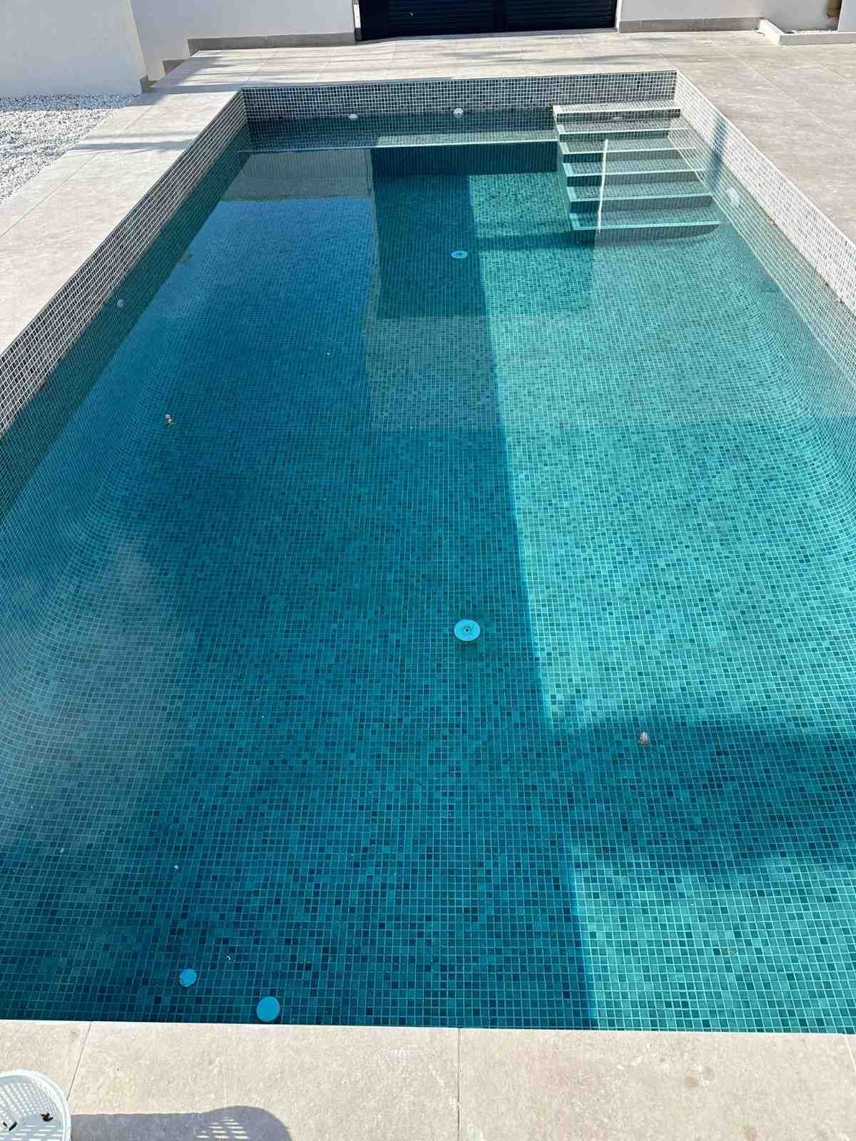 Piscina rectangular con baldosa azul verdosa, escalones y piedra clara circundante.