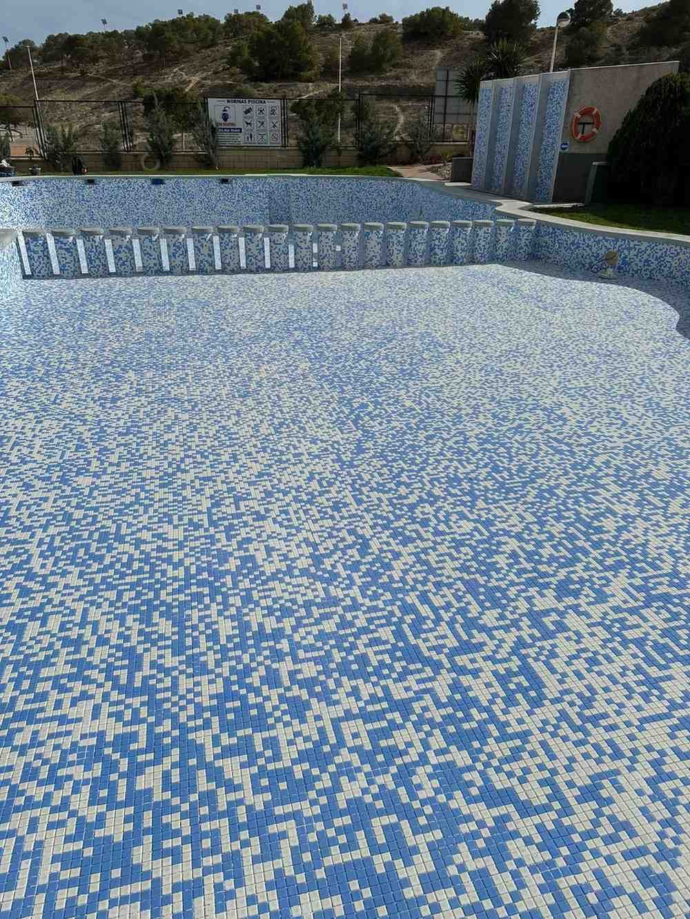 Piscina vacía de azulejos azules, al aire libre.