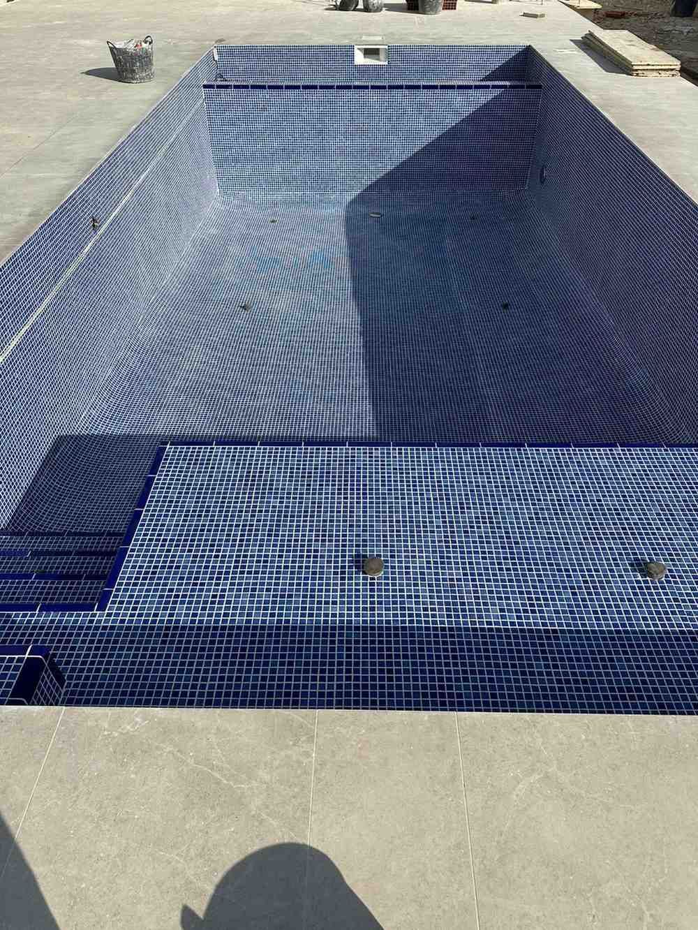 Piscina rectangular vacía revestida con mosaicos azules.
