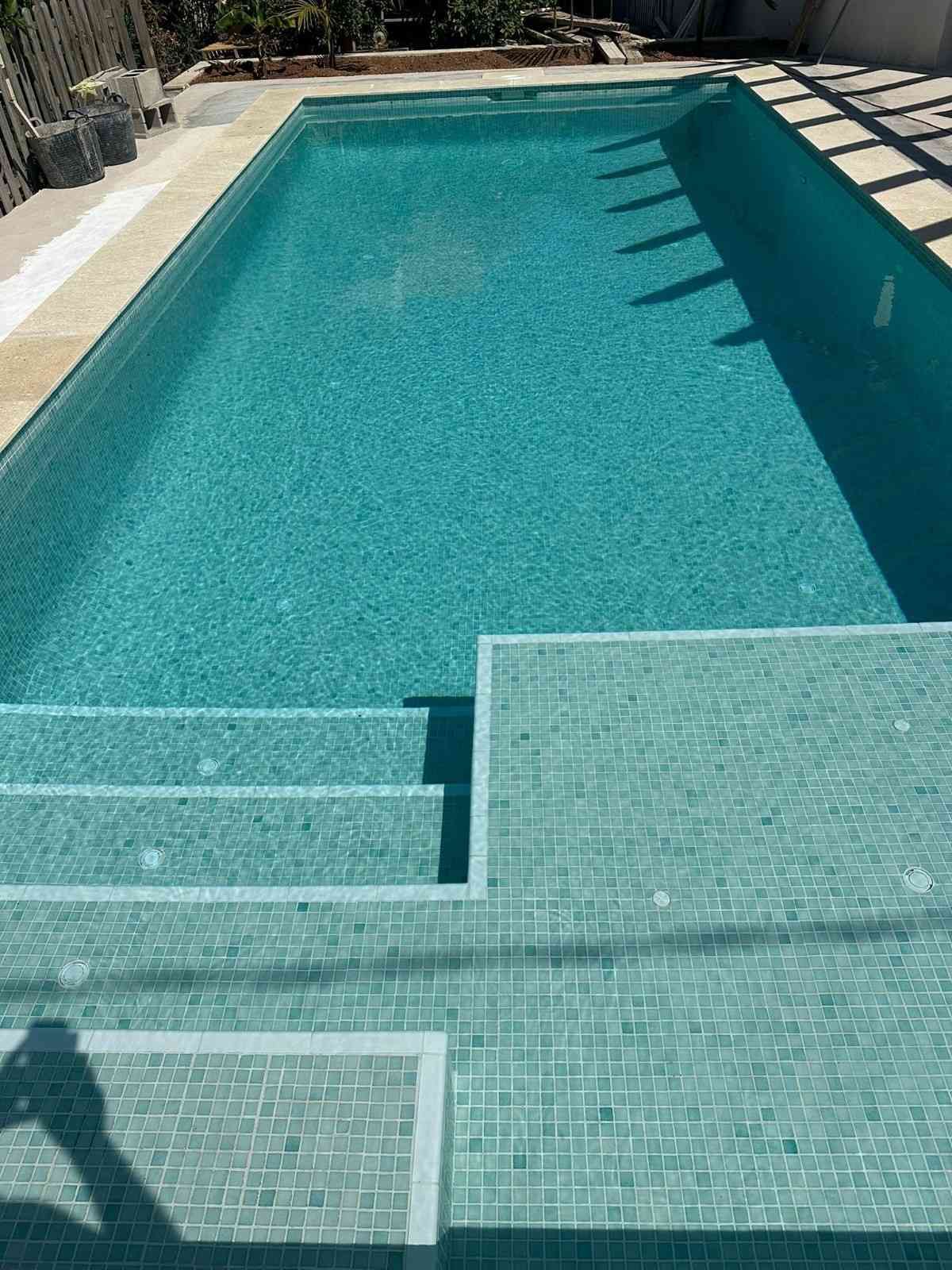 Piscina rectangular de azulejos turquesa con escalones incorporados. La luz del sol se refleja en el agua.