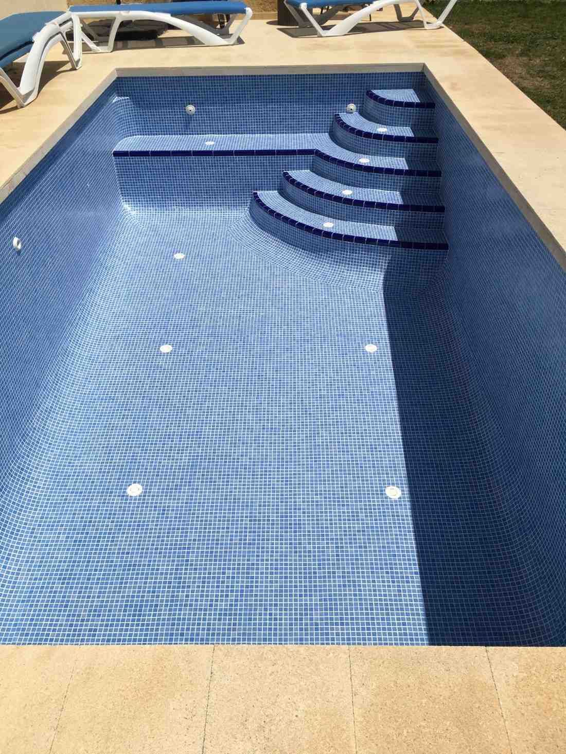 Piscina de azulejos azules con escalones, rodeada de piedra beige.