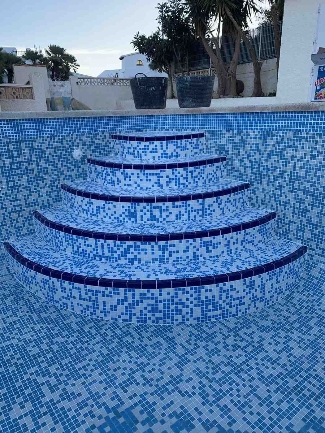 Piscina vacía con azulejos azules y blancos, escalones curvos con bordes azul oscuro.