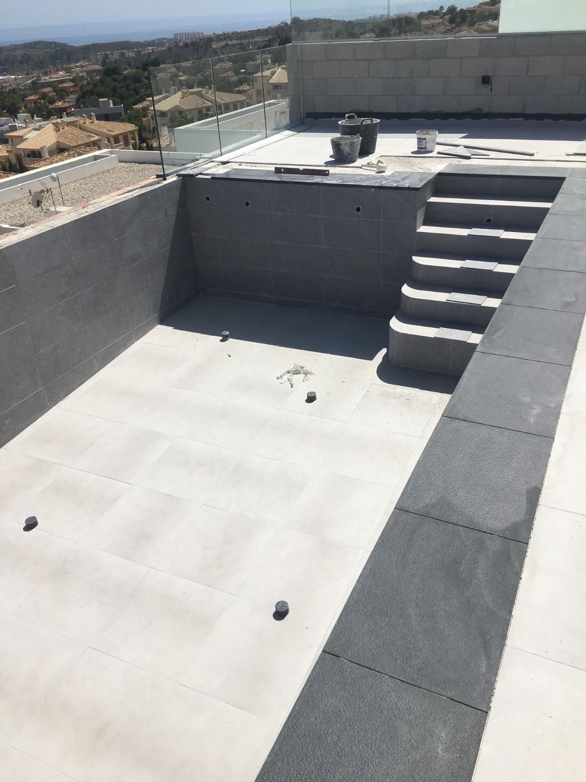 Piscina rectangular vacía en construcción, baldosas grises y blancas, escalones, entorno exterior soleado.