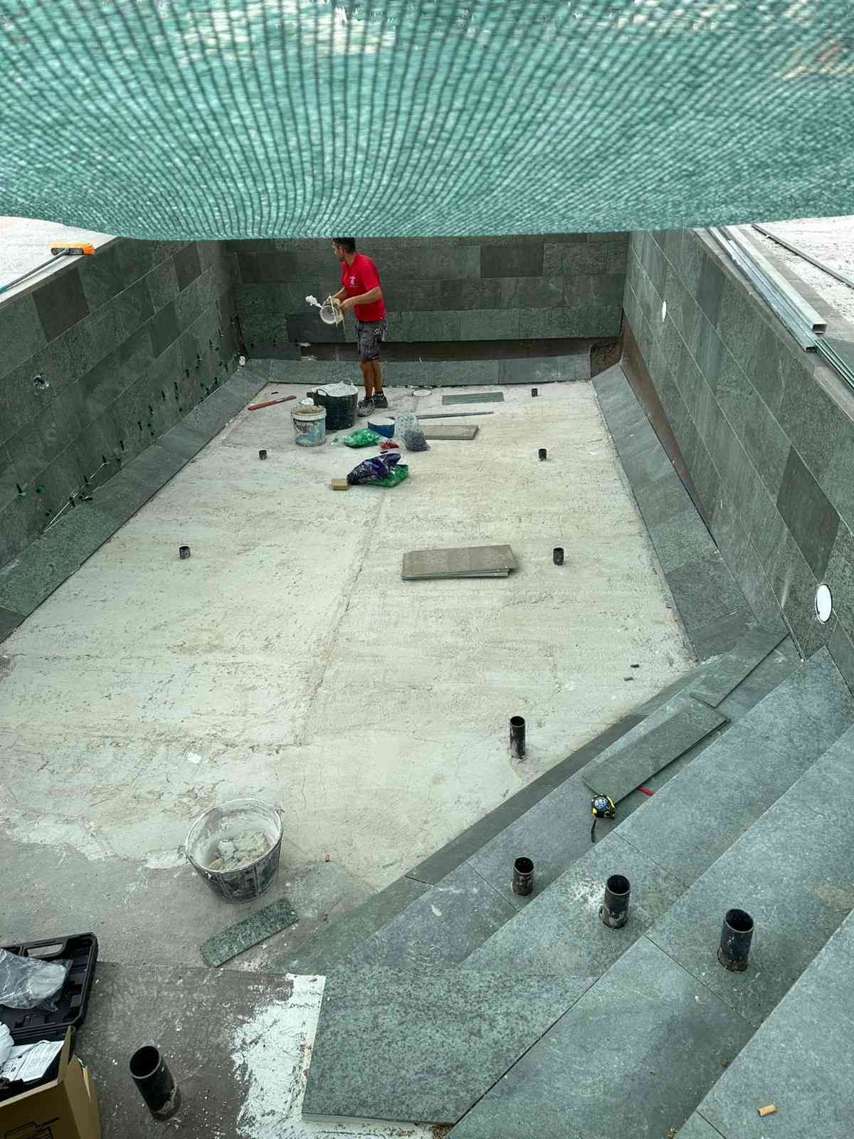 Construcción de piscina con una persona trabajando en su interior. Paredes y suelo grises, con red verde en el techo.