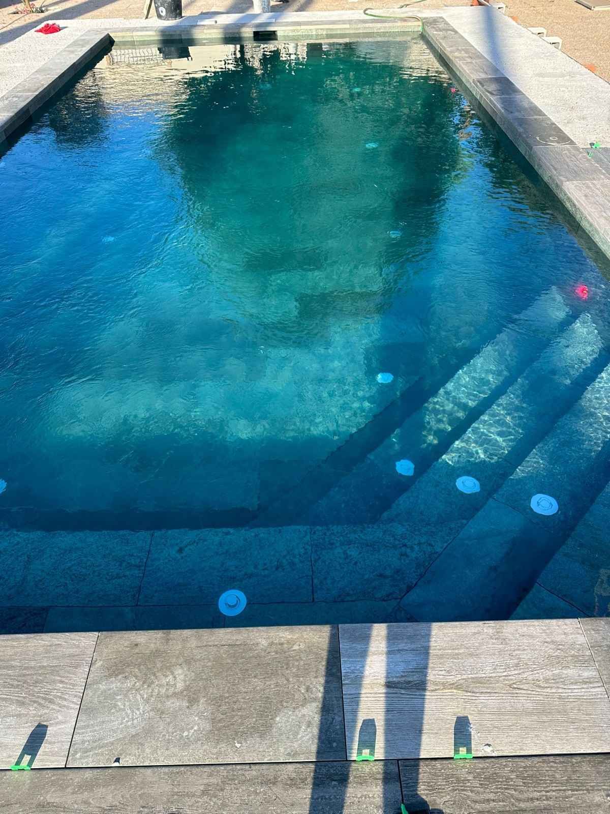 Piscina azul con escalones, rodeada de piedra. La luz se refleja en el agua.