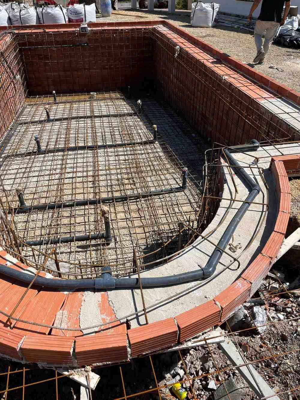 Sitio de construcción de una cimentación de piscina con borde de ladrillo, estructura de varillas de refuerzo y plomería.