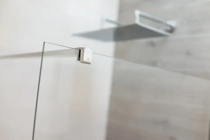 Ducha con puerta de cristal, cabezal de ducha metálico y paredes revestidas de azulejos en tonos claros.