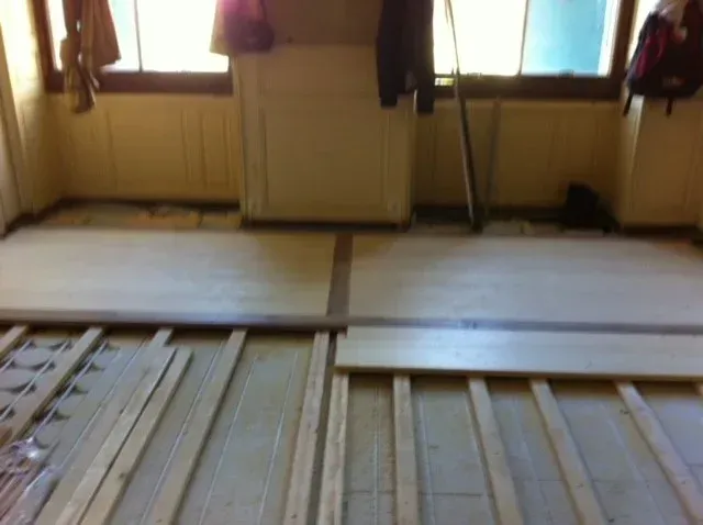 Grenier inachevé avec poutres apparentes, planches de bois au sol et un ouvrier sur la droite.