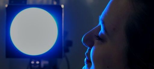 Das Profil einer Person blickt in einem dunklen Raum auf einen hellen, weißen Kreis, der von blauem Licht umrahmt ist.