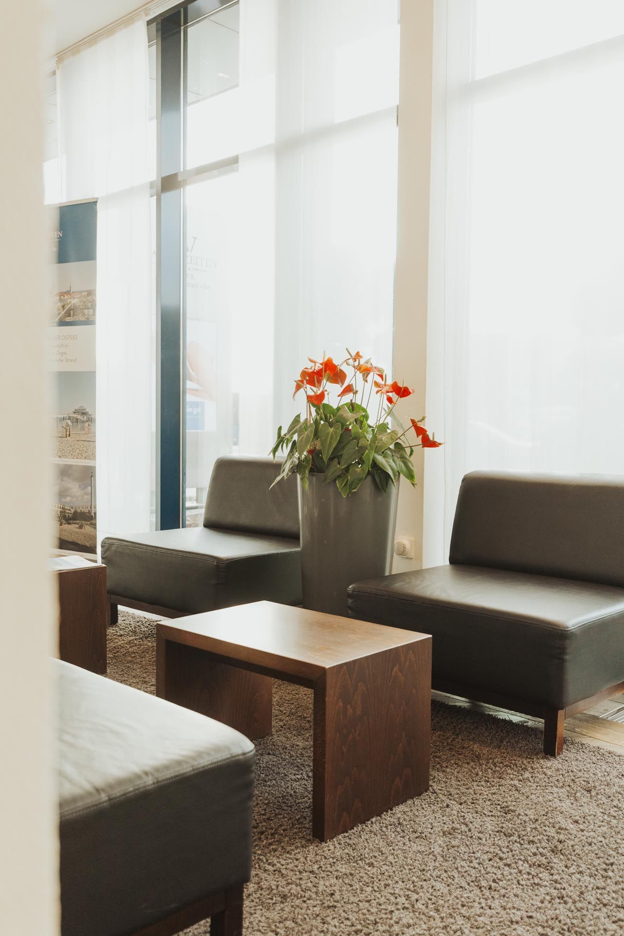 Modernes Wohnzimmer mit dunklen Sofas, Holztisch und einer Vase mit orangefarbenen Blumen an hellen Fenstern