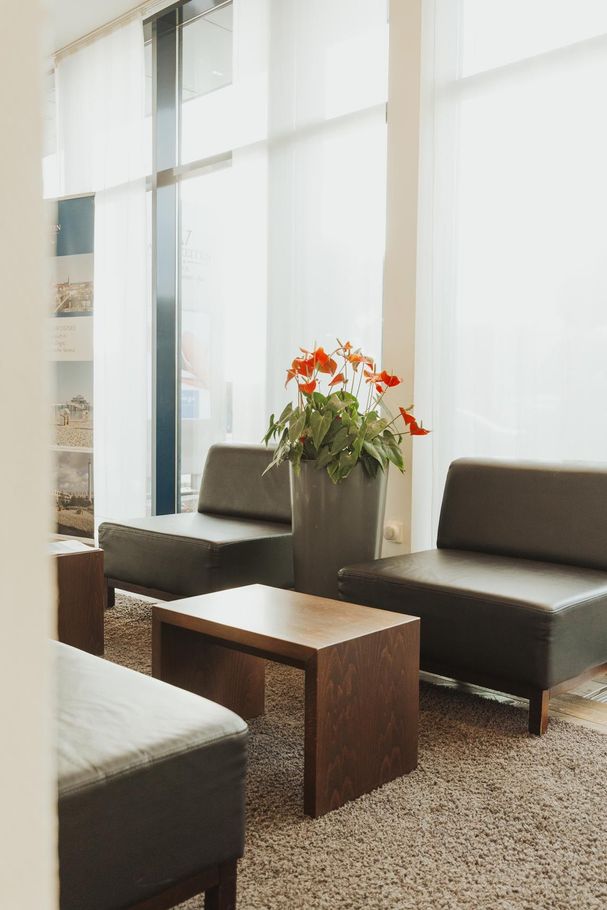 Modernes Wohnzimmer mit dunklen Sofas, Holztisch und einer Vase mit orangefarbenen Blumen an hellen Fenstern