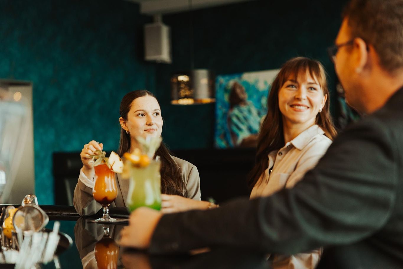 Drei Personen unterhalten sich an einem Café-Tisch, eine hält ein Orangengetränk in der Hand.