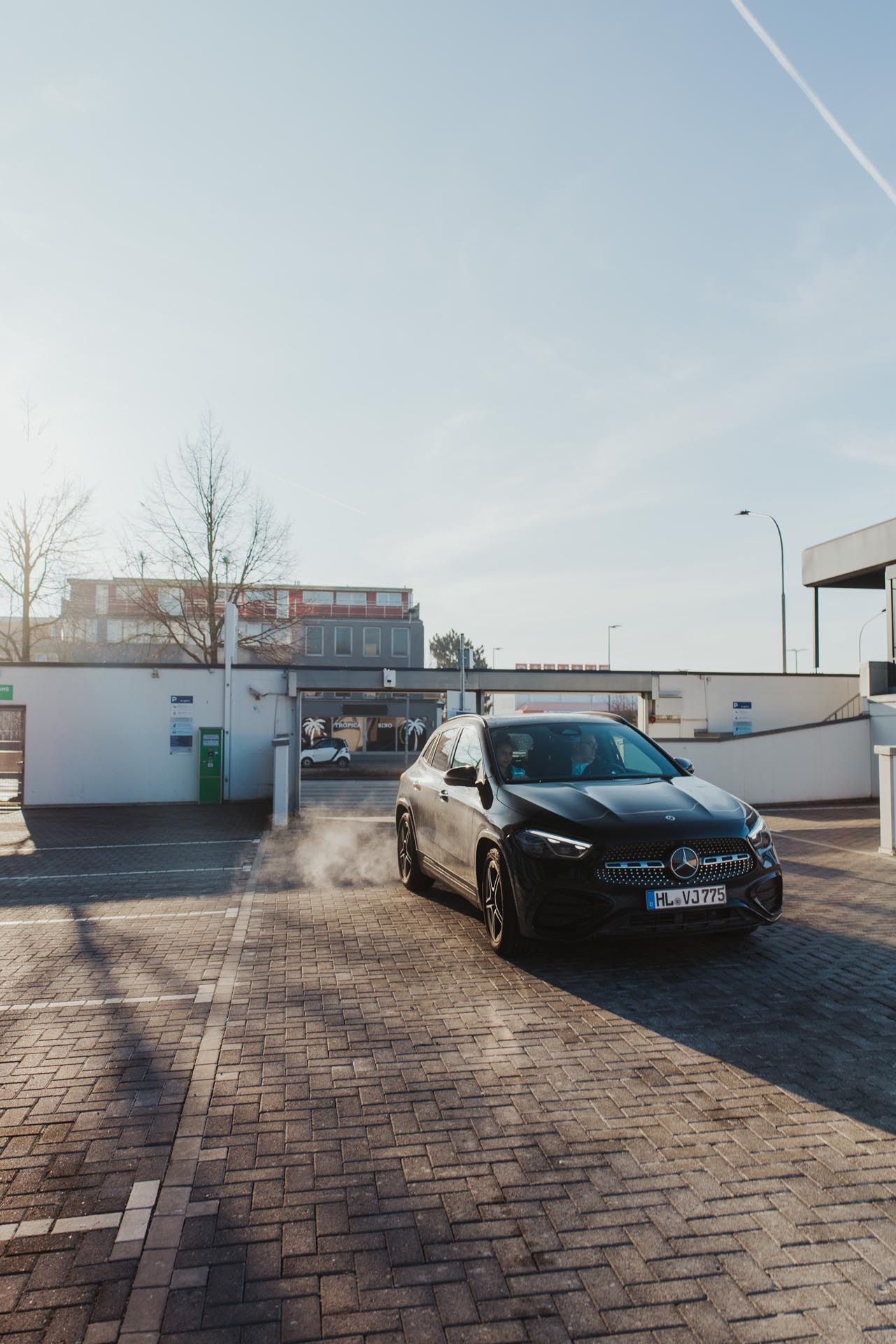 Eine schwarze Limousine parkte auf einem Kopfsteinpflasterparkplatz neben einer weißen Mauer unter klarem Himmel.