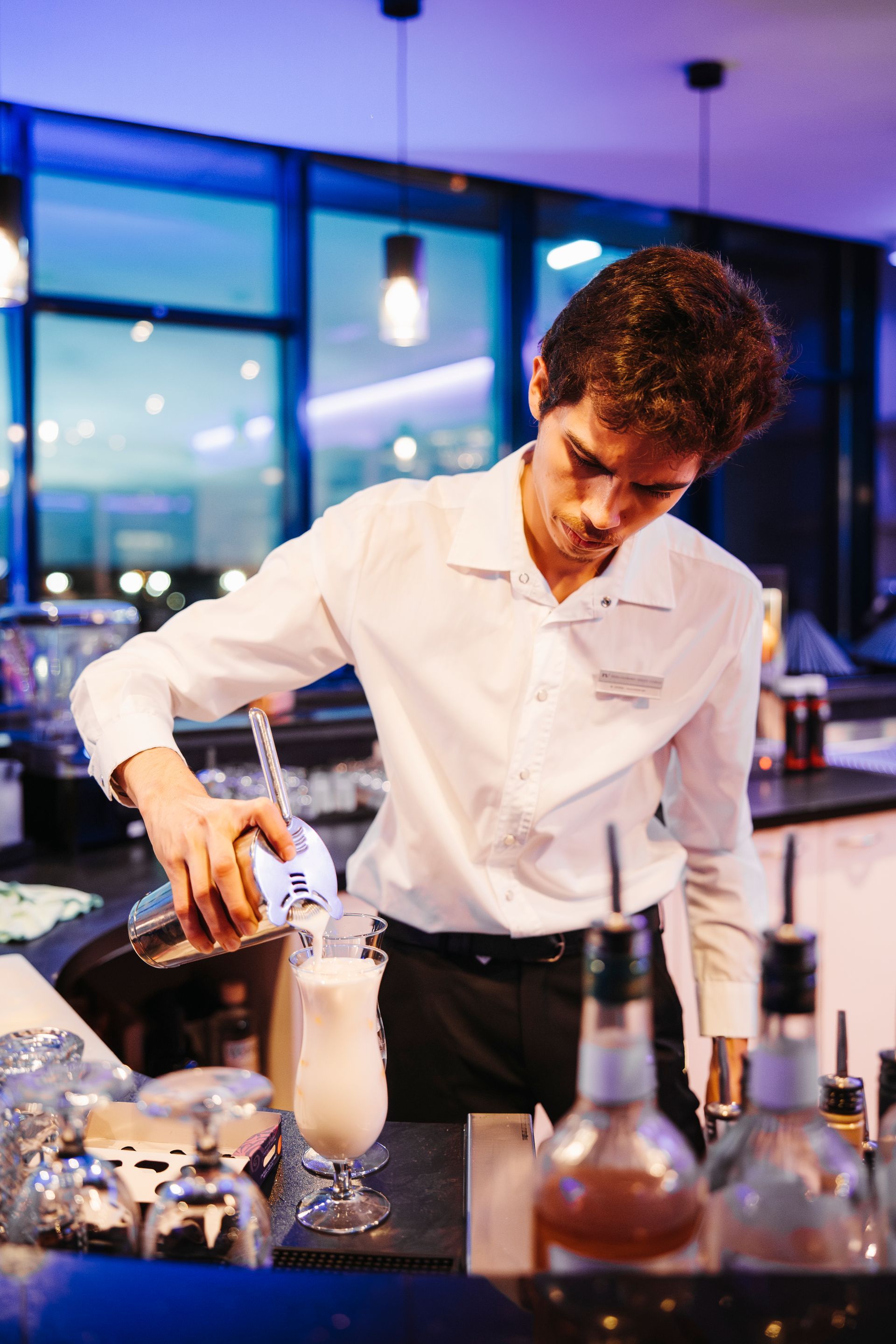 In einer Bar gießt ein Barkeeper einen Drink in ein Glas.