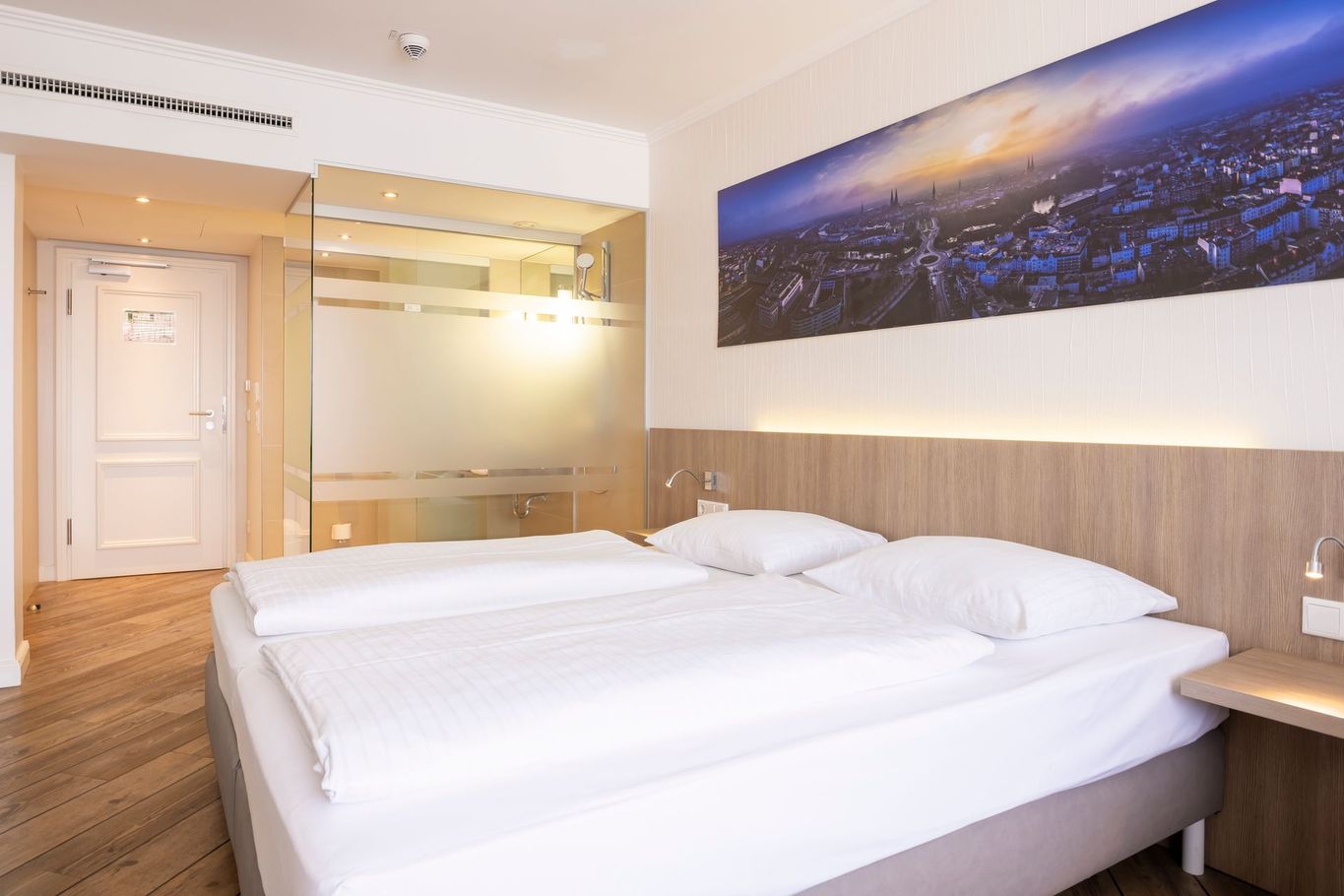 Modernes Hotelzimmer mit zwei weißen Betten, Holzböden und Wandbild mit Stadtansicht