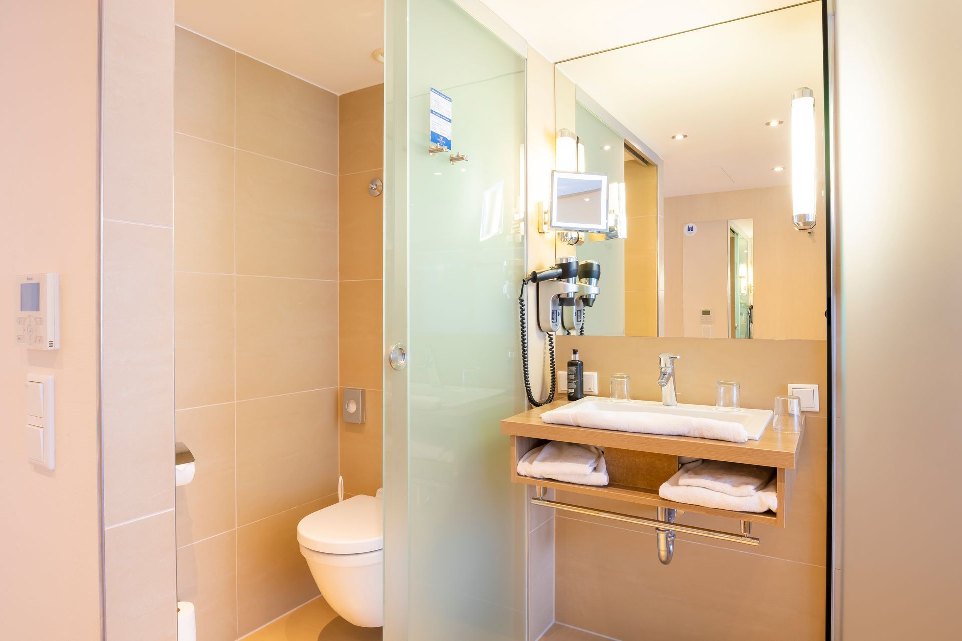 Badezimmer mit Toilette, Waschbecken, Spiegel und teilweise mattierter Glaswand. Farbgestaltung in Hellbeige und Weiß.