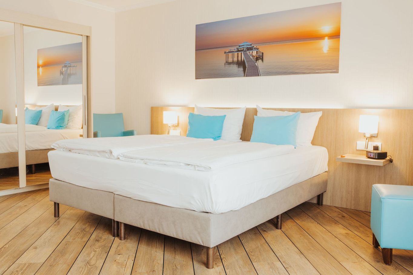 Helles, modernes Hotelzimmer mit weißem Bett, türkisfarbenen Akzenten, Holzboden.
