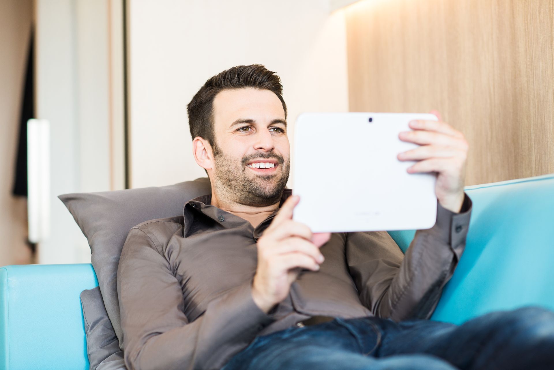 Ein Mann liegt auf einer Couch und nutzt einen Tablet-Computer.