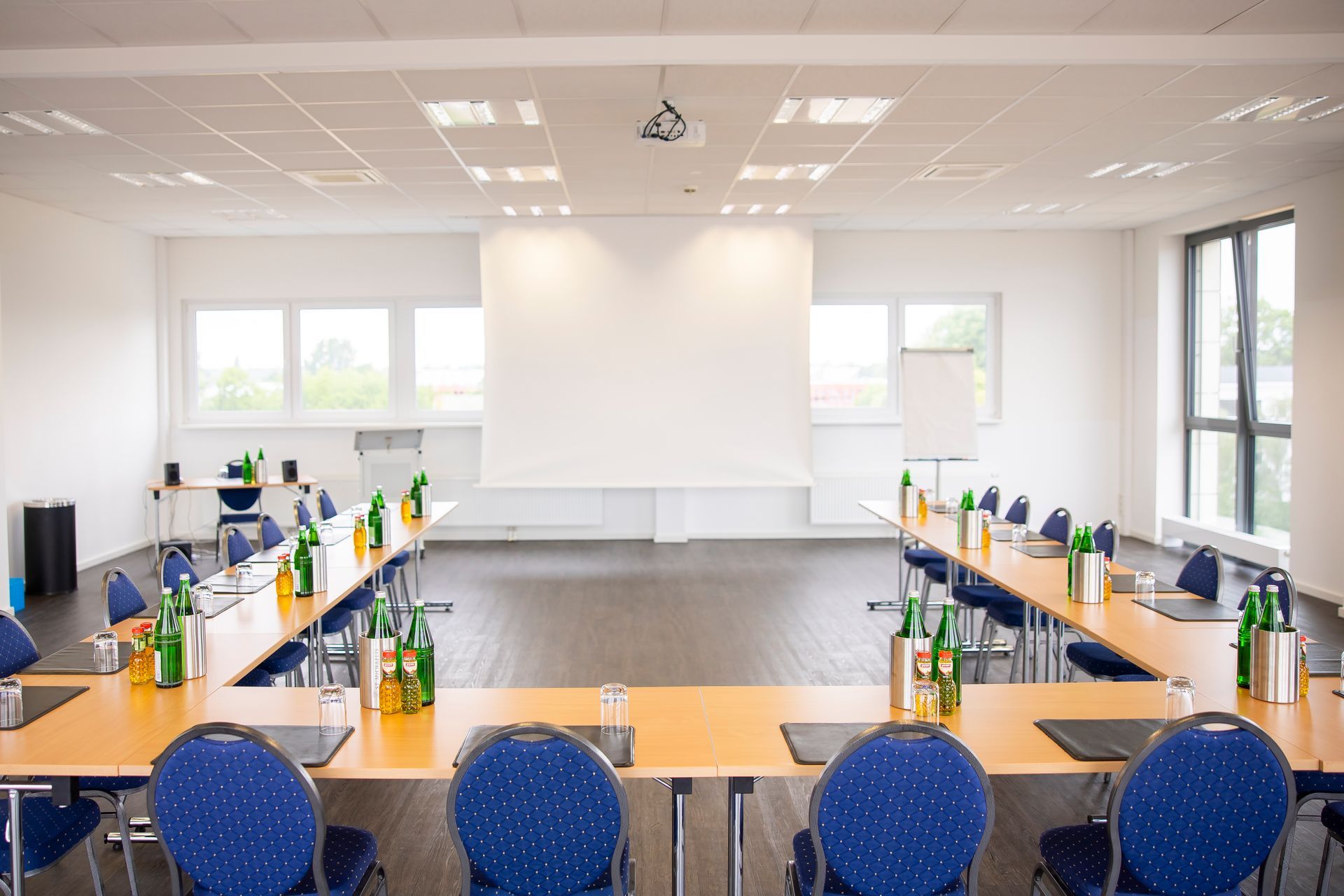 Ein Konferenzraum mit Tischen und Stühlen sowie einer Projektionsleinwand.