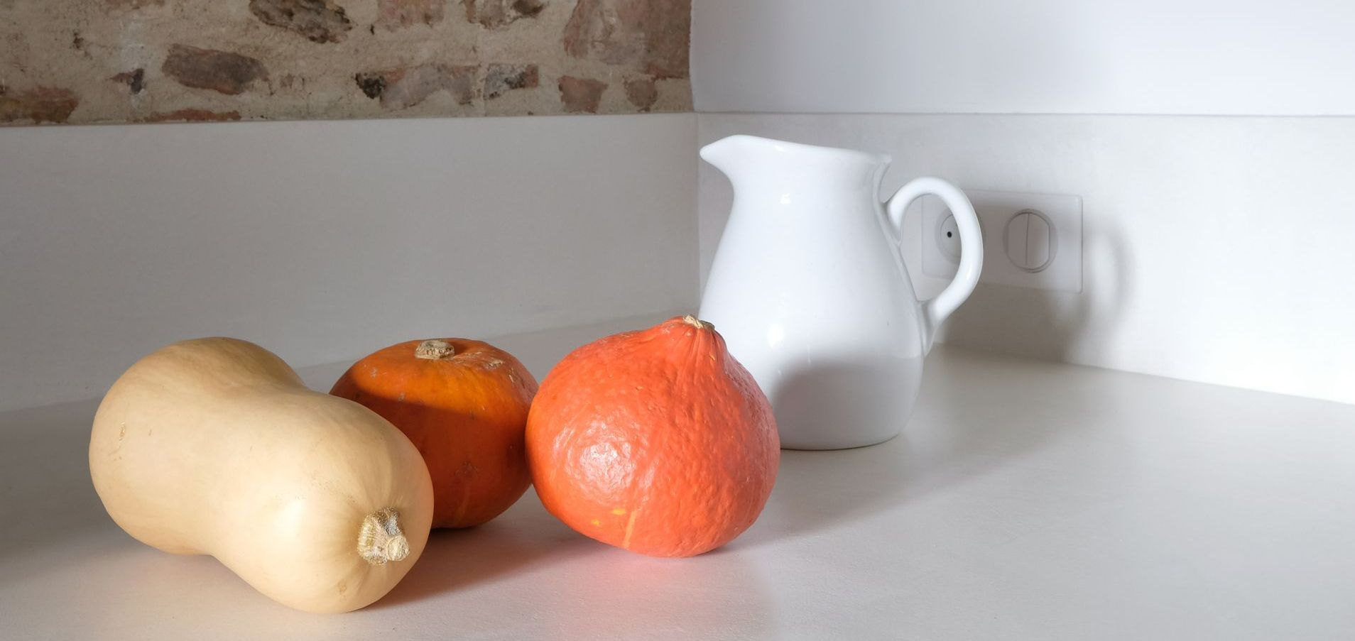 Courge et potimarrons devant une cruche sur un plan de travail