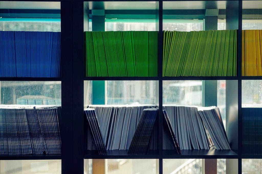 Libros en un estante, fondo de coloridas ventanas de cristal (azul, verde, amarillo) con vistas a la ciudad.