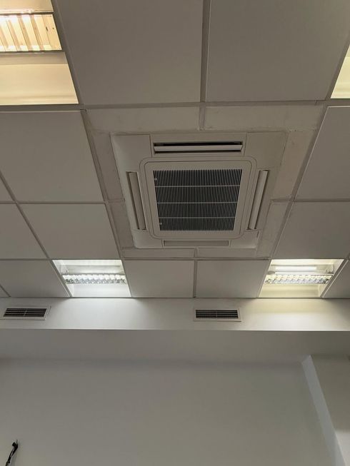 Techo de oficina con paneles de luz empotrados y una rejilla de ventilación central sobre una pared blanca.