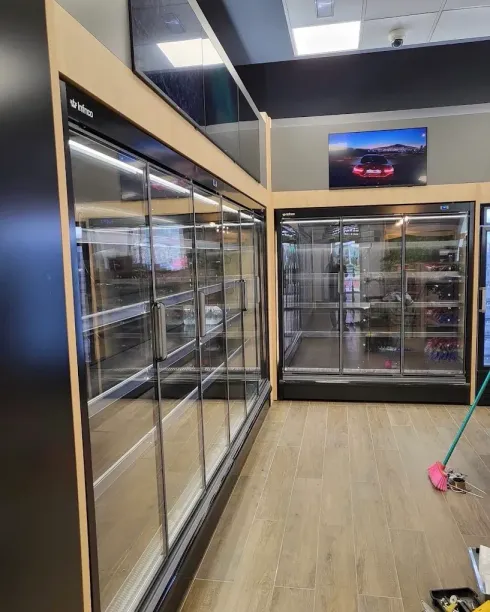 Pasillo de supermercado con refrigeradores con puertas de vidrio y un pequeño televisor montado encima.