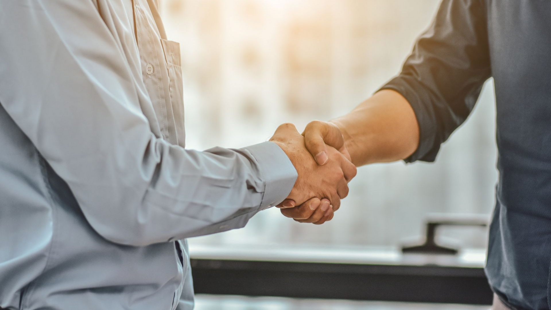 Deux personnes se serrant la main, arrière-plan flou, lumière du soleil.