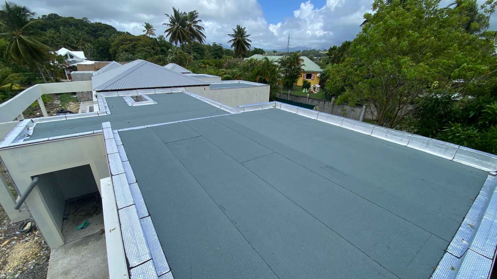 Une personne utilise une perceuse pour fixer une tôle ondulée bordeaux sur une structure en bois, à l'extérieur par temps de neige.