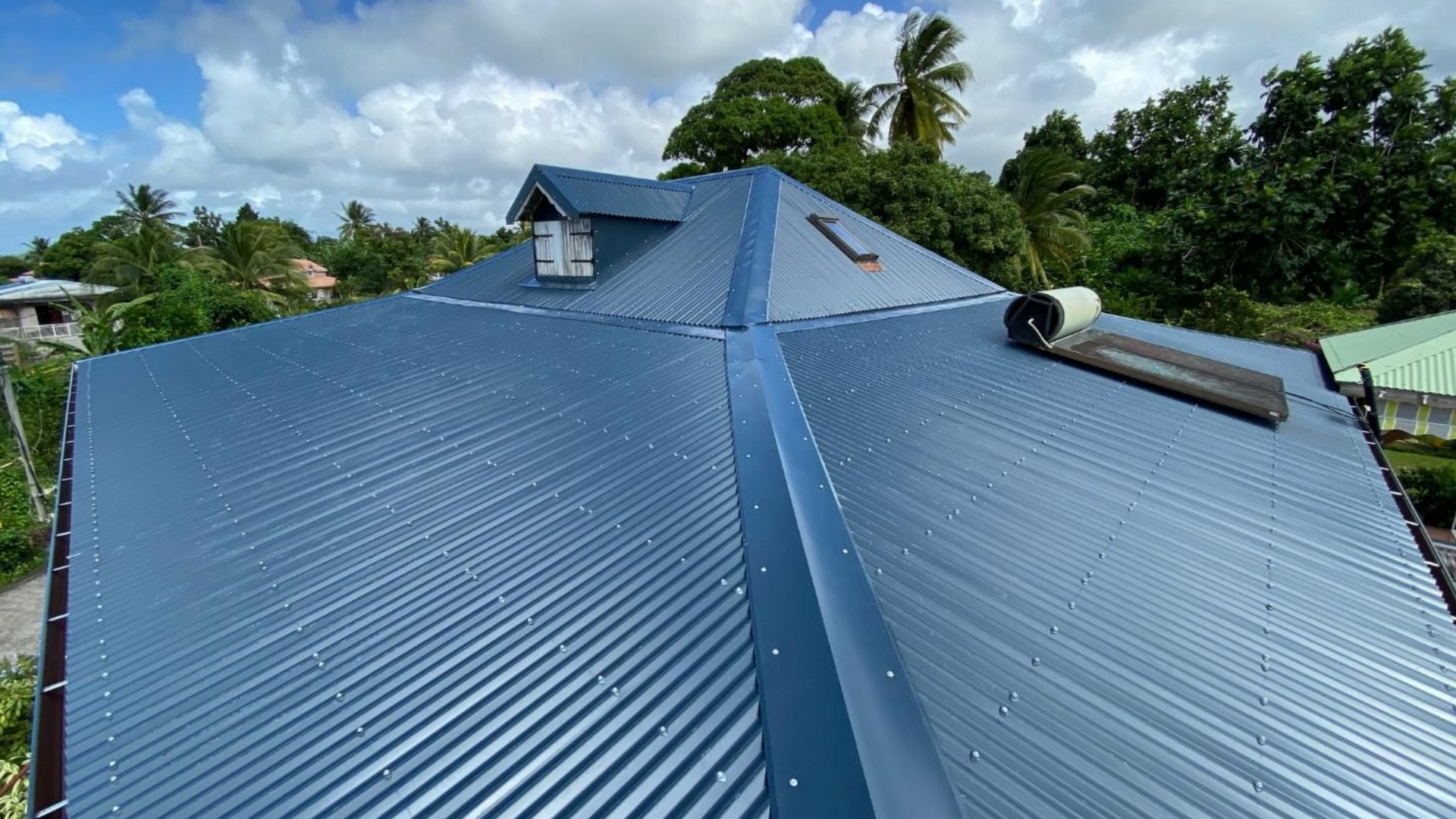Toit en métal brillant avec puits de lumière sur fond de ciel ensoleillé.
