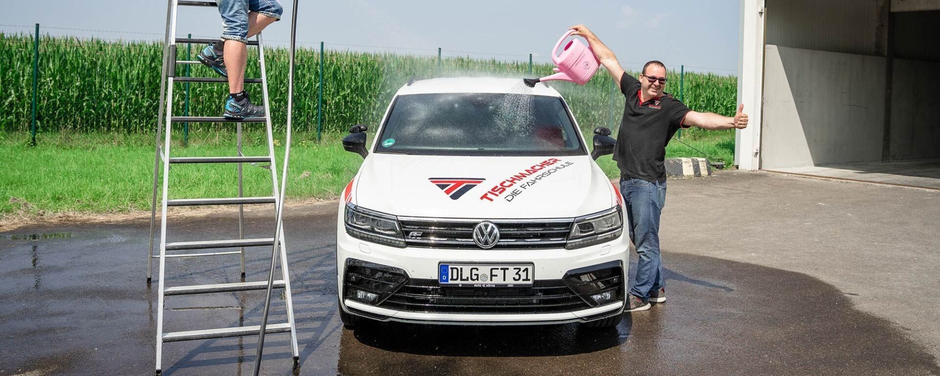 Fahrlehrer wäscht Fahrschulauto mit Giesßkanne