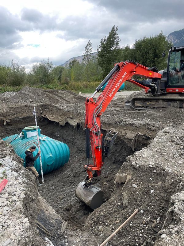 Cuve de récupération d'eau au fond d'un trou creusé par une tractopelle rouge.