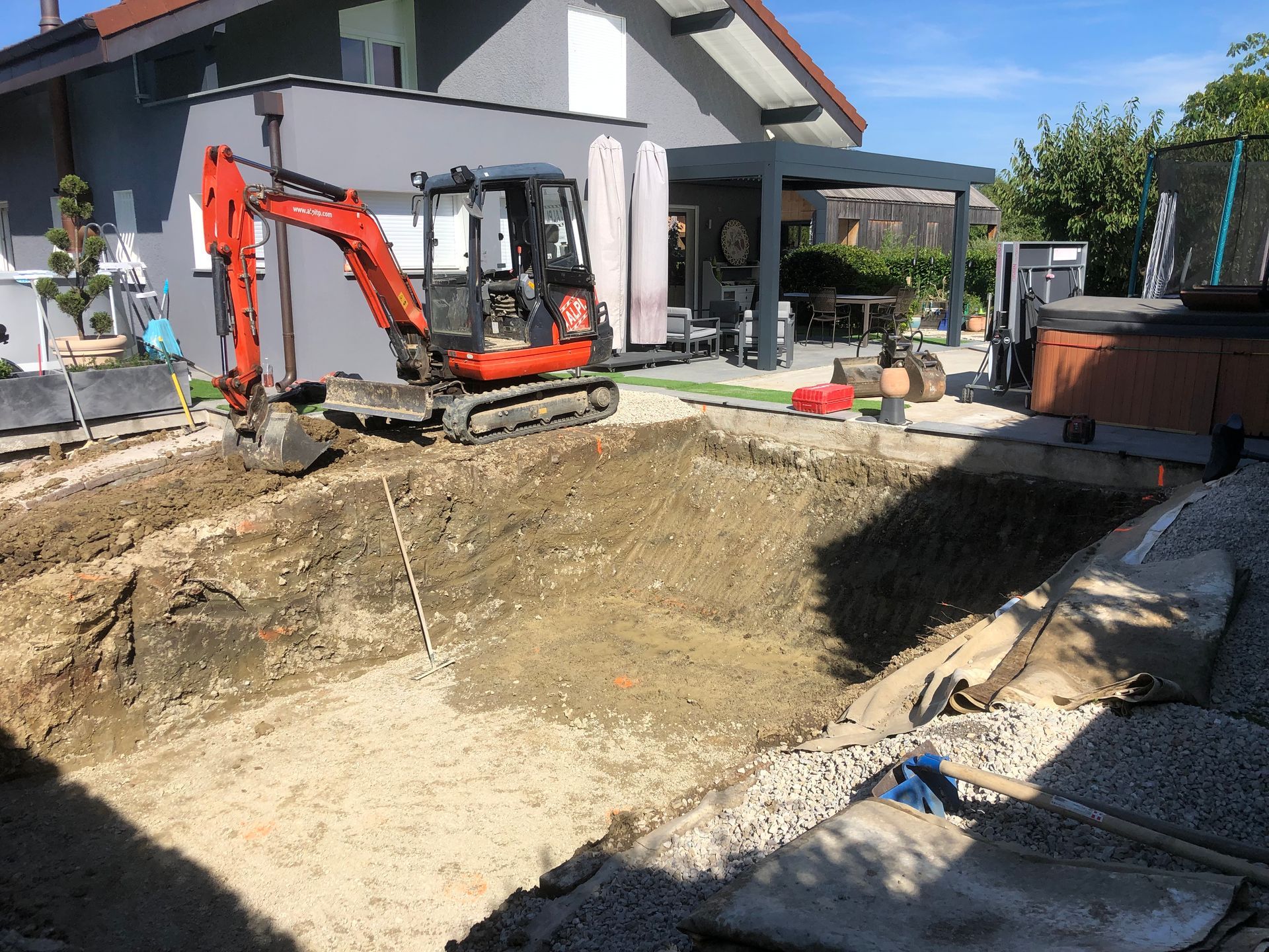 Engin de chantier rouge qui creuse une piscine près d'une habitation.