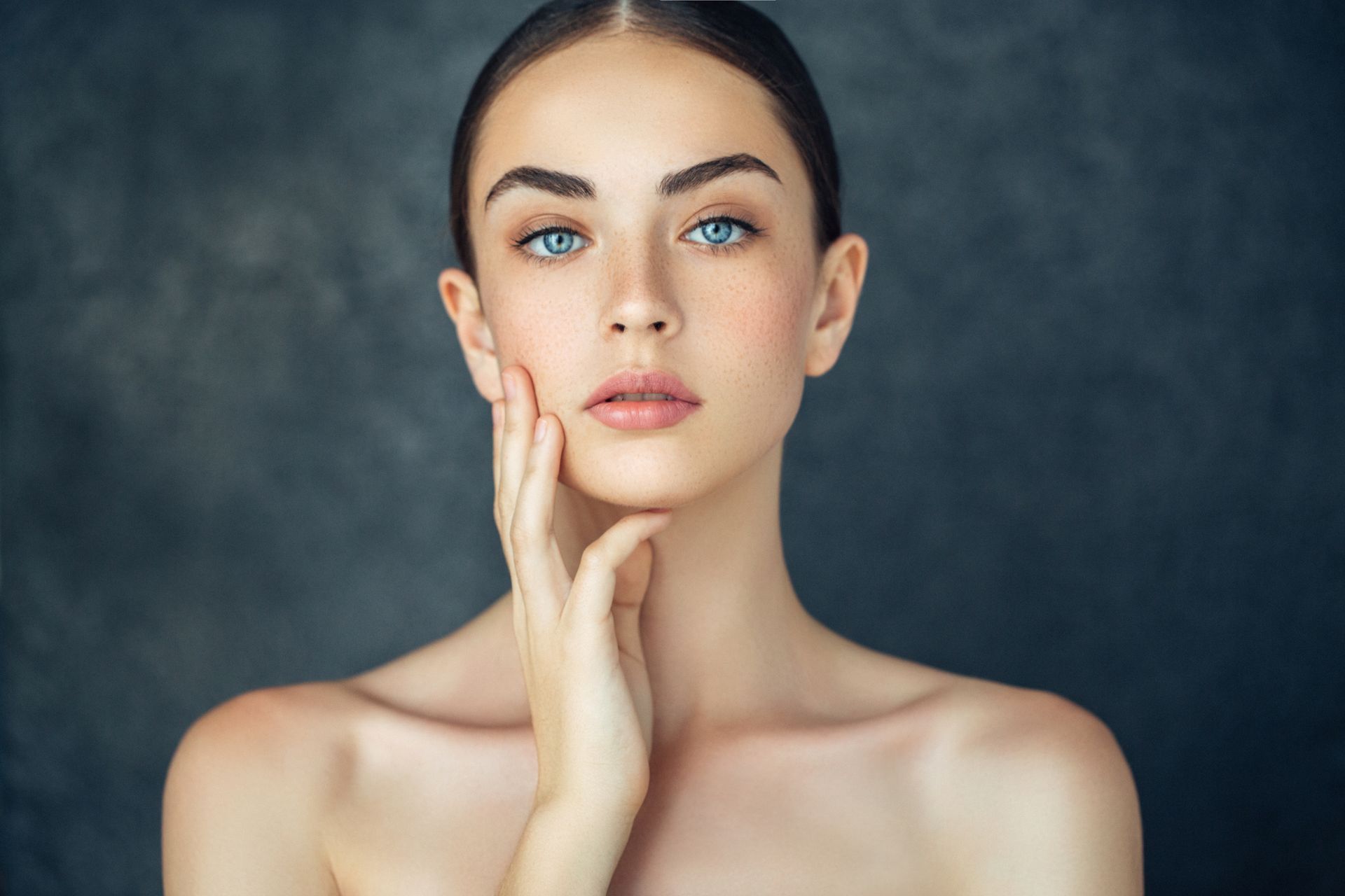 Una mujer de ojos azules se toca la cara con la mano.