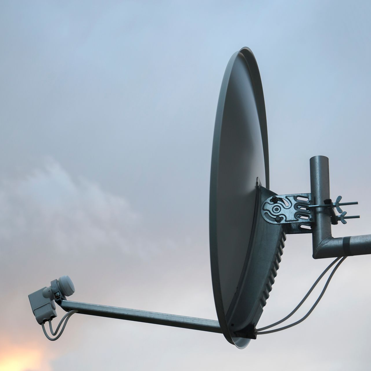 Antenne parabolique fixée sur un mât, se détachant sur un ciel nuageux.