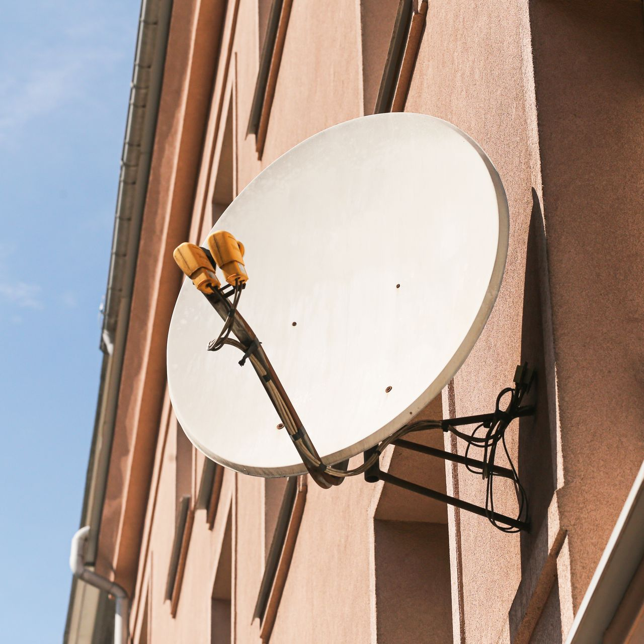 Antenne parabolique fixée sur la façade rose d'un bâtiment, orientée vers le ciel.