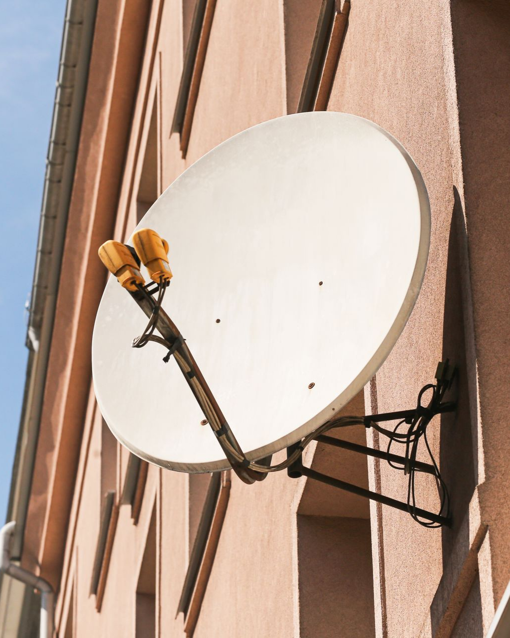 Antenne parabolique fixée sur un mur extérieur rose, orientée vers le ciel.