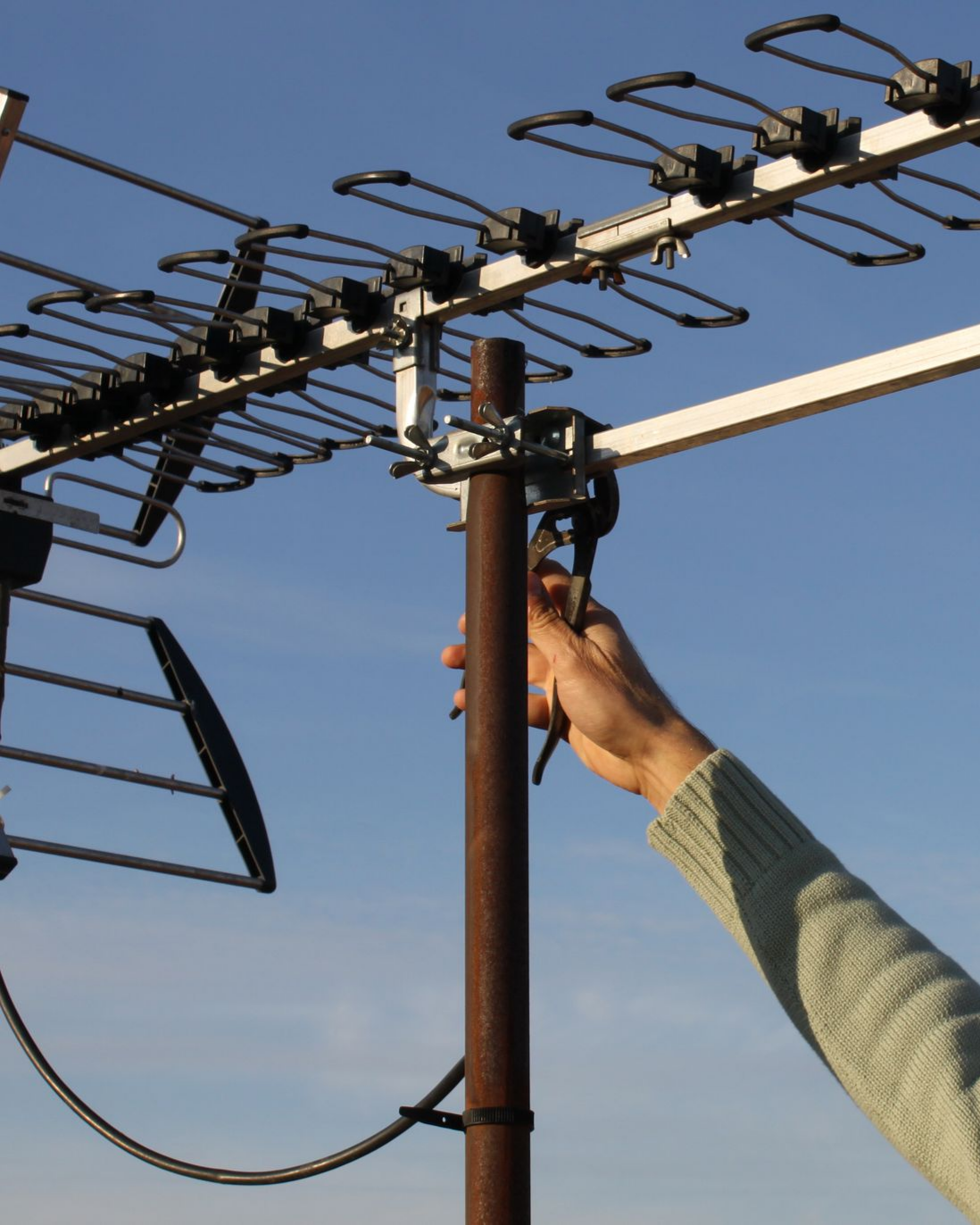 Une personne fixe une antenne de télévision sur un poteau marron, se détachant sur un ciel bleu.