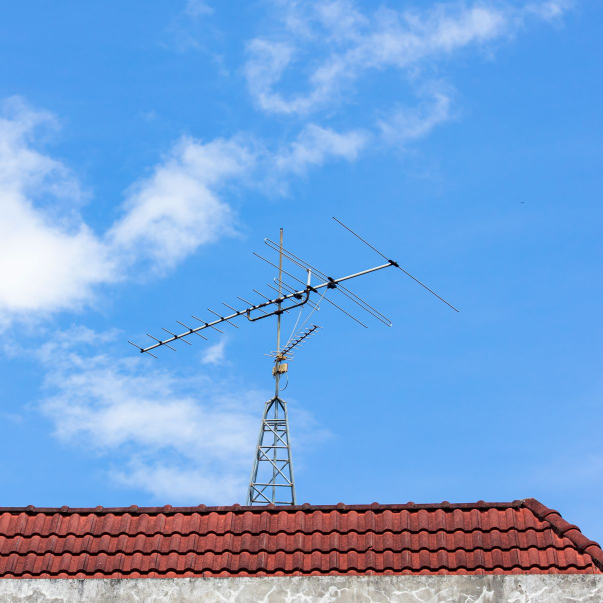 Antenne de télévision sur un toit de tuiles rouges, se détachant sur un ciel bleu.