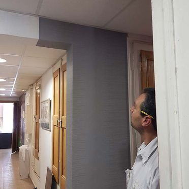 Hombre mirando una pared gris recién pintada. Pasillo con puertas abiertas.