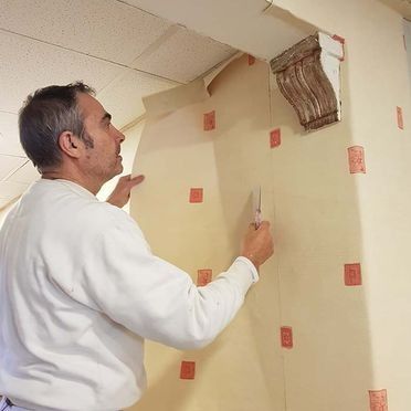 Hombre empapelando una pared con marcadores cuadrados rojos cerca de un elemento arquitectónico decorativo.