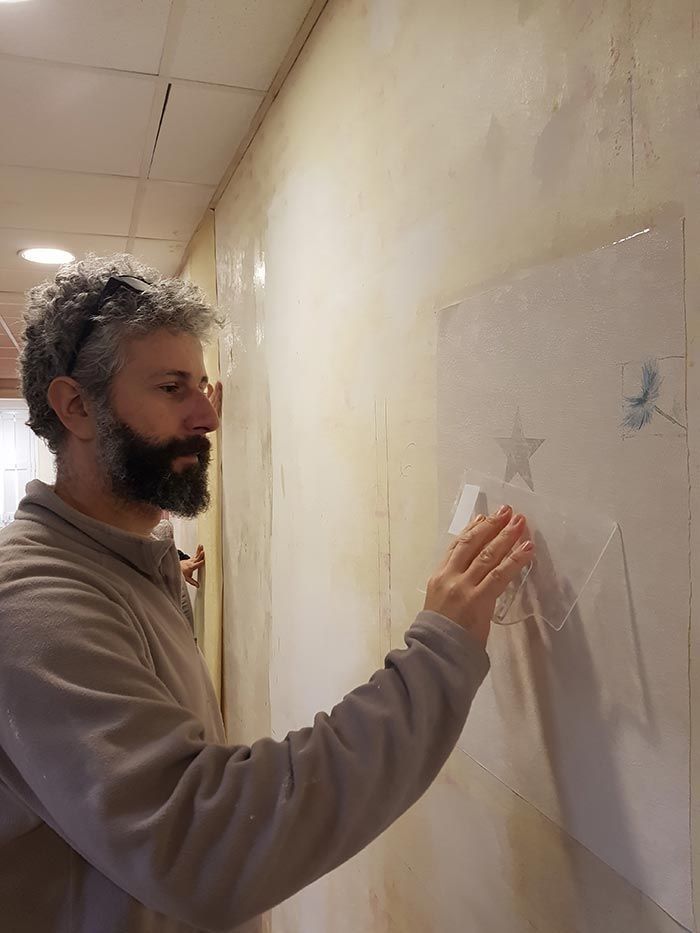 Hombre con barba gris tocando una plantilla en una pared texturizada.