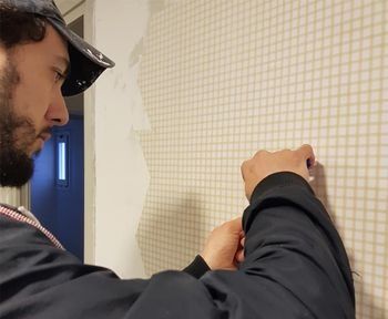 Un hombre con gorra quita el papel pintado con motivos cuadriculados de una pared.