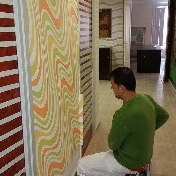 Un hombre con un suéter verde pinta una pared con un patrón ondulado.